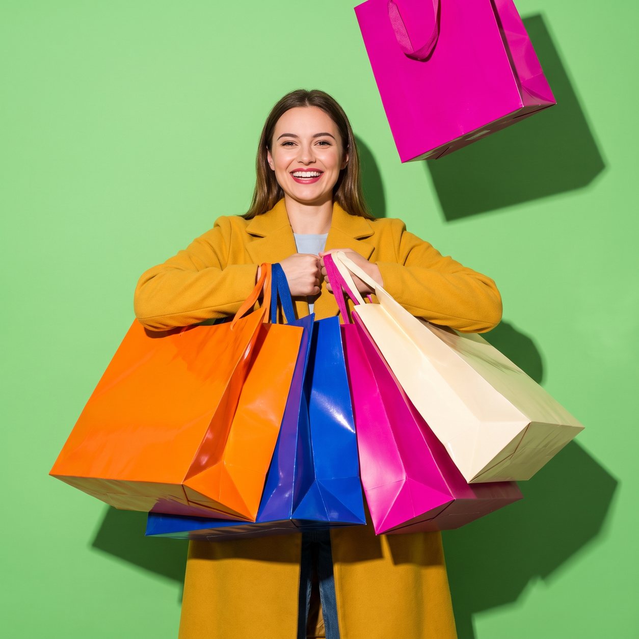 A smiling woman in a mustard coat holds an armful of glossy oversized shopping bags in orange, cobalt, magenta and cream, against a lime-green backdrop.