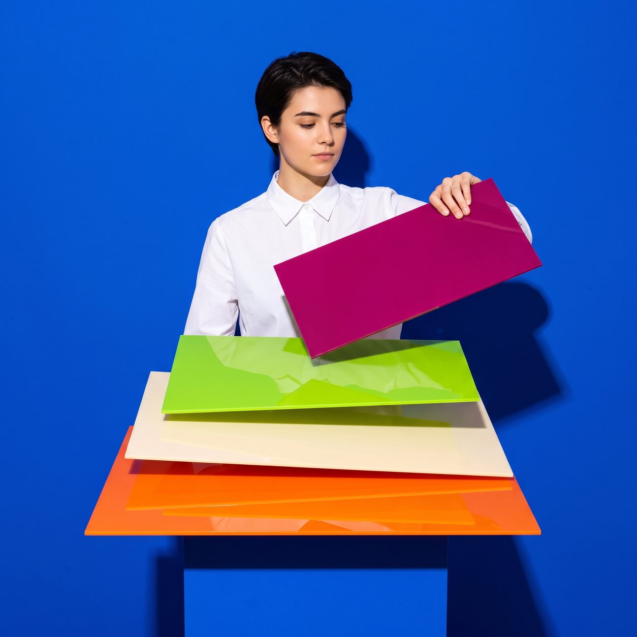 A designer in a white shirt stacks large glossy colour-block panels like the sections of a web page, against a cobalt-blue backdrop.