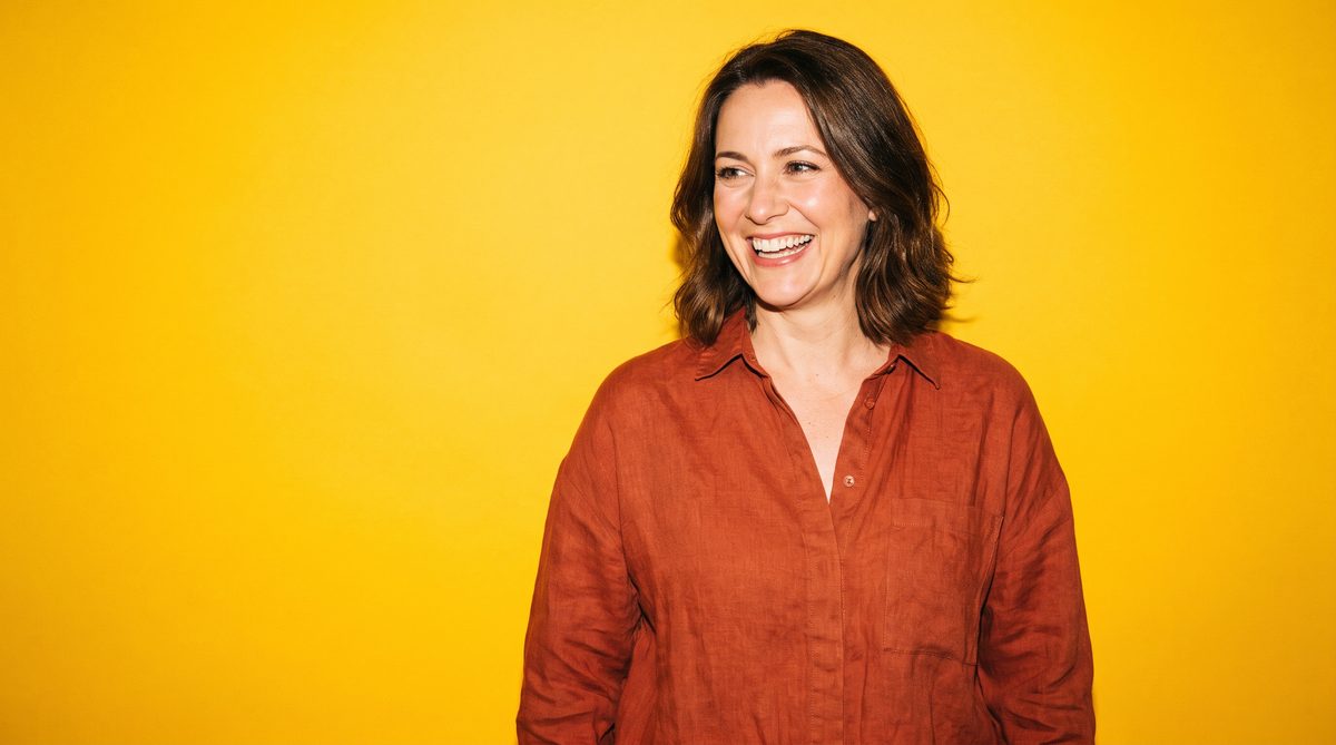 A laughing business owner in a terracotta linen shirt against a sunny yellow backdrop